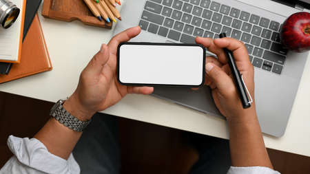 Cropped shot of professional businessman holding blank screen smartphone over his office desk.の写真素材