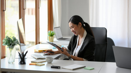 Female business owner or entrepreneur checking her business sale report on a clipboard at her desk.の写真素材