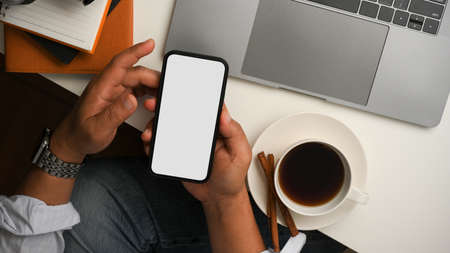 Businessman or male freelancer is using smartphone, scrolling on social media in his coffee break at table.の写真素材