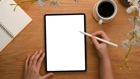 Top view, close-up shot of a female's hand drawing on digital tablet computer over wooden table.の写真素材
