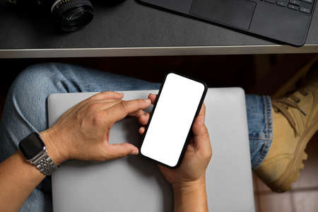 Top view of hipster man holding blank screen smartphone in modern workplace with laptop.の写真素材