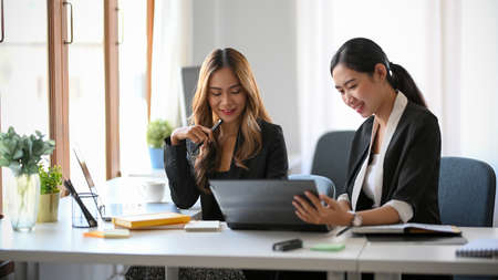 Two businesswomen looking some informations on the documents folder at their office workplace.の写真素材