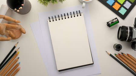 Empty notepad, school notebook or spiral notepad on workspace table with stationery, camera, colour...