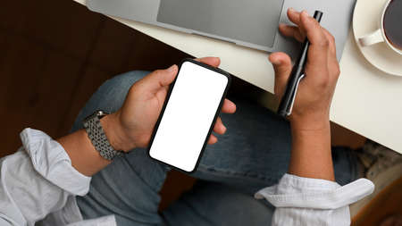 Successful businessman sitting at his office desk and using mobile phone to check his market stock....