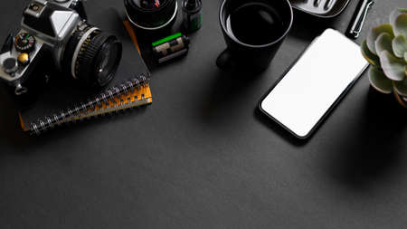 Professional freelance photographer working desk with retro camera, films, lens, smartphone blank screen mockup and copy space on black background. top viewの写真素材