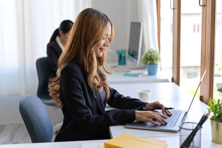 Beautiful Asian businesswoman typing on laptop computer, planning her project details in the office.の写真素材