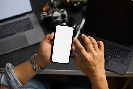 Close-up image of an adult man holding a smartphone blank screen mockup over modern office desk. Top viewの写真素材