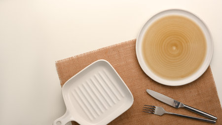 Flat lay, an empty plate with empty small white pan plate and silverware on placemat over white background.の写真素材