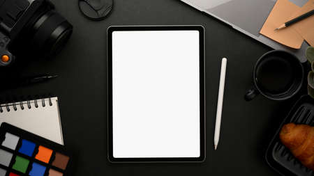 Tablet touchscreen with blank display mockup on a modern black workspace with photographer or graphic designer work tools. Top viewの写真素材
