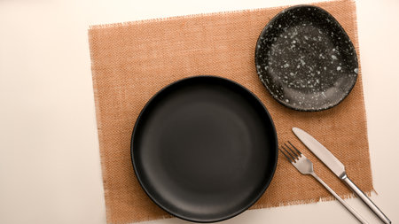 Modern minimal dark kitchenware with empty black plate and silverware over placemat on white background. space for text and menu. top viewの写真素材