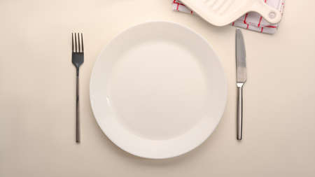 Empty simple white ceramic plate with silverware on white table, top view, flat layの写真素材