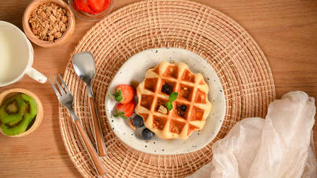 Homemade waffle served with honey syrup and fresh berries, warm milk and granola on a wooden table.の写真素材