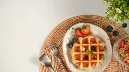Yummy homemade waffle with berries and honey syrup on a plate served on white table with copy space.の写真素材