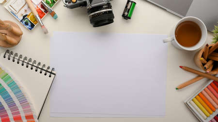 Graphic designer workspace with colour swatch samples, watercolour palette, oil pastel colour, camera and empty blank paper on table. top viewの写真素材