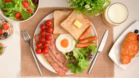 Top view, English breakfast set with egg, hams, sausages, toasts, croissant, milk and salad on table.の写真素材