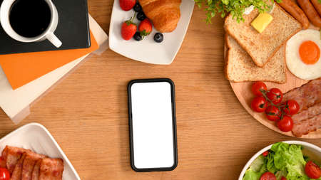 A smartphone blank screen mockup on a table with breakfast. Template mockup for your graphic image, food application or your restaurant banner.の写真素材