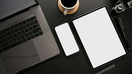 Modern dark workspace with laptop computer, smartphone and digital tablet white screen mockup for...
