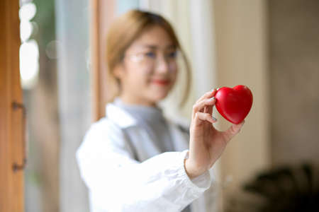 Selective focus image, A female doctor in white coat holding a heart model in her clinic.