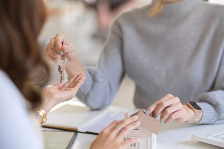 Close-up image of a female realtor giving a house key chain to new tenant in the office workplace.の写真素材