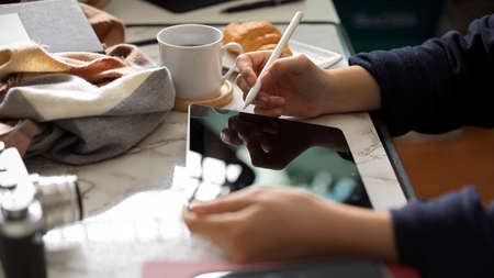 Side view, a female freelancer using a digital tablet touchpad computer with stylus pen at her desk.