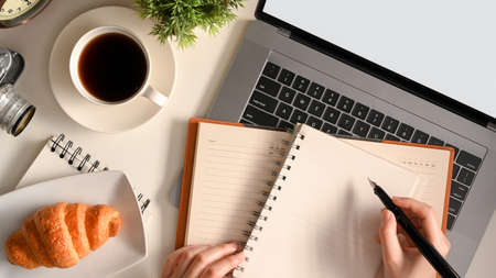 A female taking notes on her diary book over her laptop computer on modern workspace. top viewの写真素材