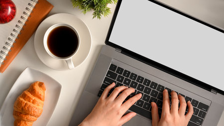 A female or businesswoman working on laptop computer at her modern workspace with croissant and coffee for breakfast. top viewの写真素材