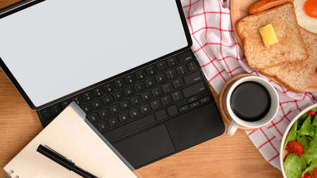 Top view of a modern workspace with digital tablet computer, notebook, coffee cup and breakfast set.の写真素材