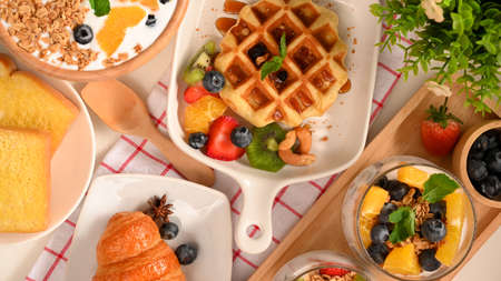 Dessert or sweets concept. Waffle with berries, yogurt bowl, croissant and toasts on minimal table.の写真素材