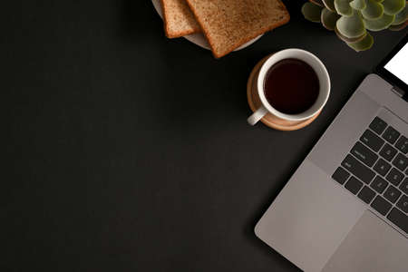 Modern black workspace background with laptop computer, coffee cup toasts and copy space. top viewの写真素材