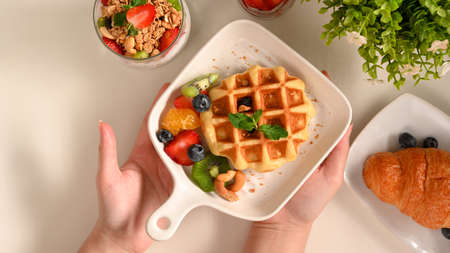 Overhead shot of a female's hands holding a plate of dessert over table. waffle with fresh berries.の写真素材