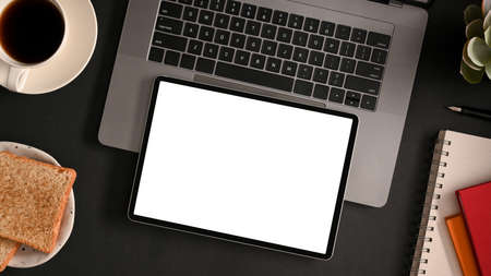 Mockup screen of a digital tablet computer on laptop computer over modern black workspace design.の写真素材