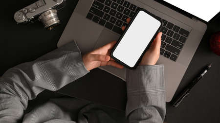 Overhead shot of a businesswoman texting on her smartphone during working on laptop computer at her...