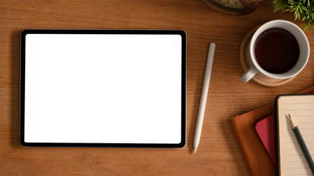 Simple wooden worktable with white screen tablet computer, stylus pen, coffee cup and stationery.の写真素材