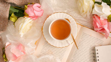 Top view of a beautiful feminine workspace with novel book, tea cup and roses flowers decorations. Women's desk and hobby conceptの写真素材