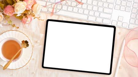 Beautiful female office workspace with digital tablet computer blank screen mockup, tea cup, keyboard and decorations. top viewの写真素材