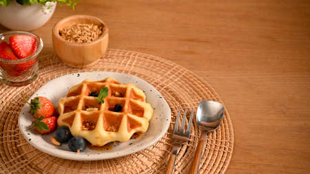 Sweets, pastries, bakery concept. Homemade waffle with syrup and fresh berries on bamboo placemat over wooden table with copy space.の写真素材