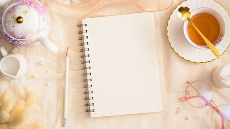 Beautiful girly workspace with blank empty diary book, tea cup, pencil and decorations on table.の写真素材