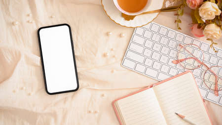 Stylish women's desk, office workspace with smartphone blank screen mockup, notebook, keyboard, tea cup, eye-glasses and decor. top viewの写真素材