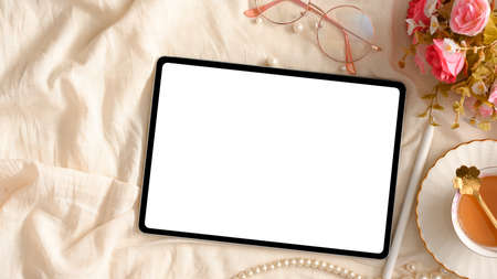 Female's workspace with tablet touchpad computer mockup, roses flowers bouquet, tea cup and eye-glasses on white background. top viewの写真素材
