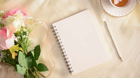 Empty notebook with pencil, tea cup and roses flowers on white table. Feminine workspace concept.の写真素材