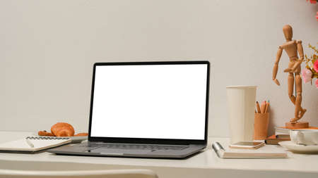 Minimal office workspace with laptop computer blank screen mockup, stationery, decor on table over white wall background.の写真素材