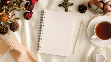 Top view, Feminine workspace background with empty spiral notebook, tea cup, vintage clock, dried flowers and sweater on white background. Winter, autumn compositionsの写真素材