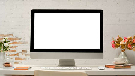 Modern office desk with pc desktop computer white screen display, office supplies, decor on table over white brick wall.の写真素材