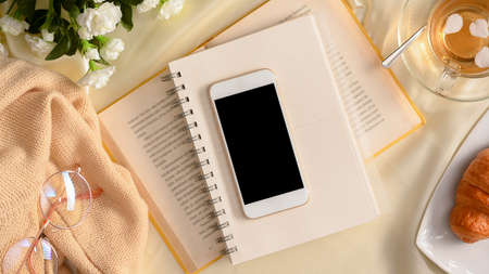 Minimal feminine workspace top view concept, Smartphone black screen on novel books, tea set, eye-glasses and decor. top view, flat layの写真素材