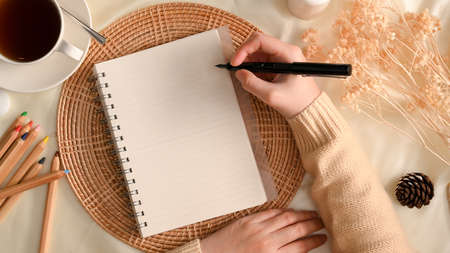 Overhead shot of a female taking notes on notepad in minimal feminine workspace decor. Cozy autumn feminine workspace conceptの写真素材