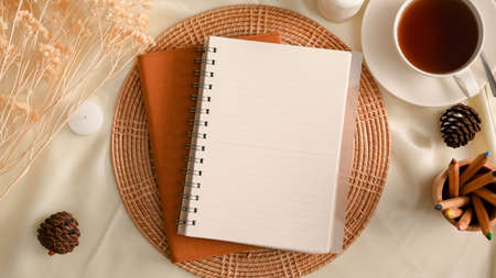 Empty spiral notebook mockup on cozy female workspace with tea cup, stationery and dried flowers. top view, flat layの写真素材