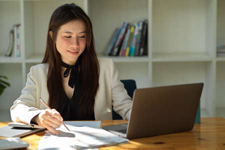 Positive and charming Asian businesswoman working on notebook laptop computer in her office workplace.の写真素材
