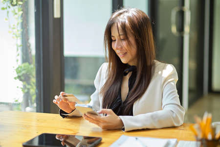 Beautiful young Asian businesswoman enjoy online shopping using credit card or debit card to pay via online payment application.の写真素材