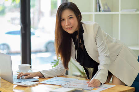 Elegant Asian businesswoman, executive manager leaning on table and working on financial statement data report in the modern office.の写真素材