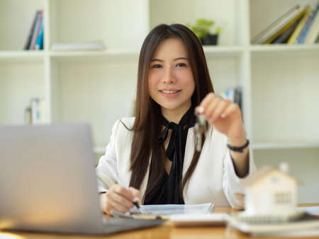Smile and positive Asian businesswoman or real estate agent holding a house keys at her office desk.の写真素材